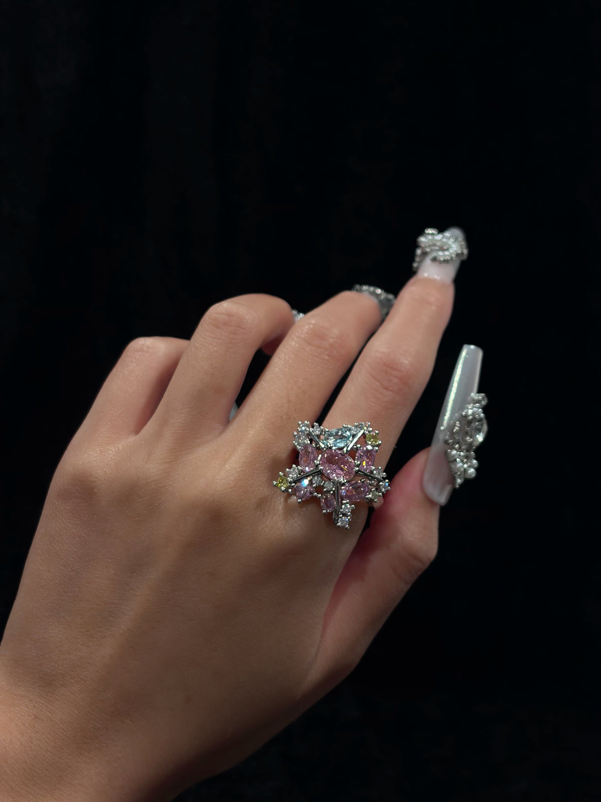Hand wearing the Aurora Star Y2K sparkling adjustable crystal star ring with multicolor cubic zirconia against a dark background