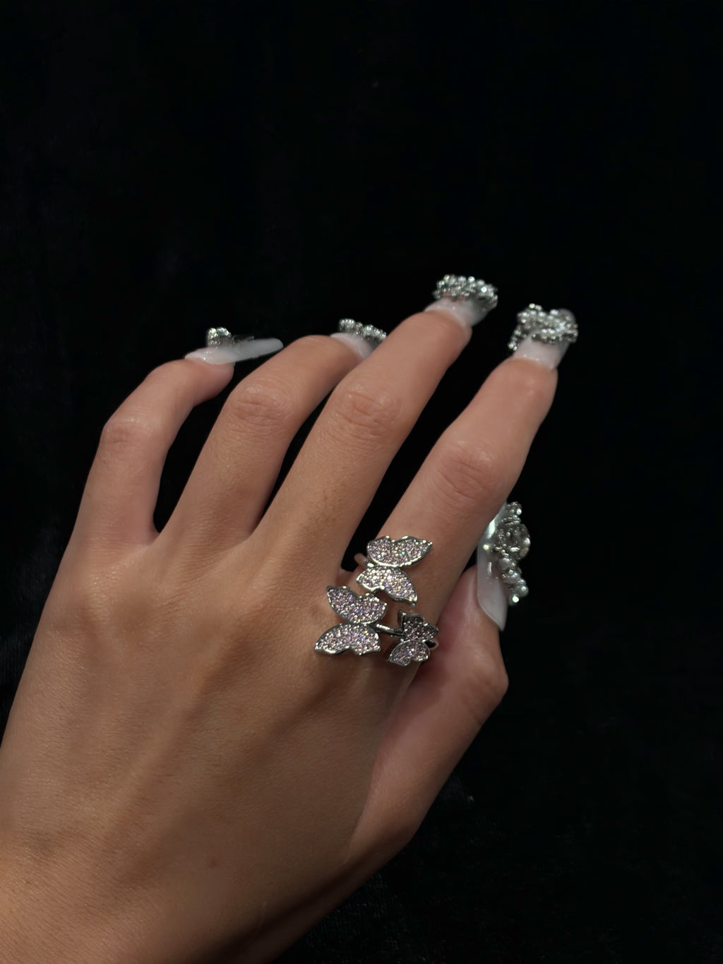 Hand wearing the Blush Butterfly Y2K sparkling adjustable ring with pink cubic zirconia butterfly details against a dark background
