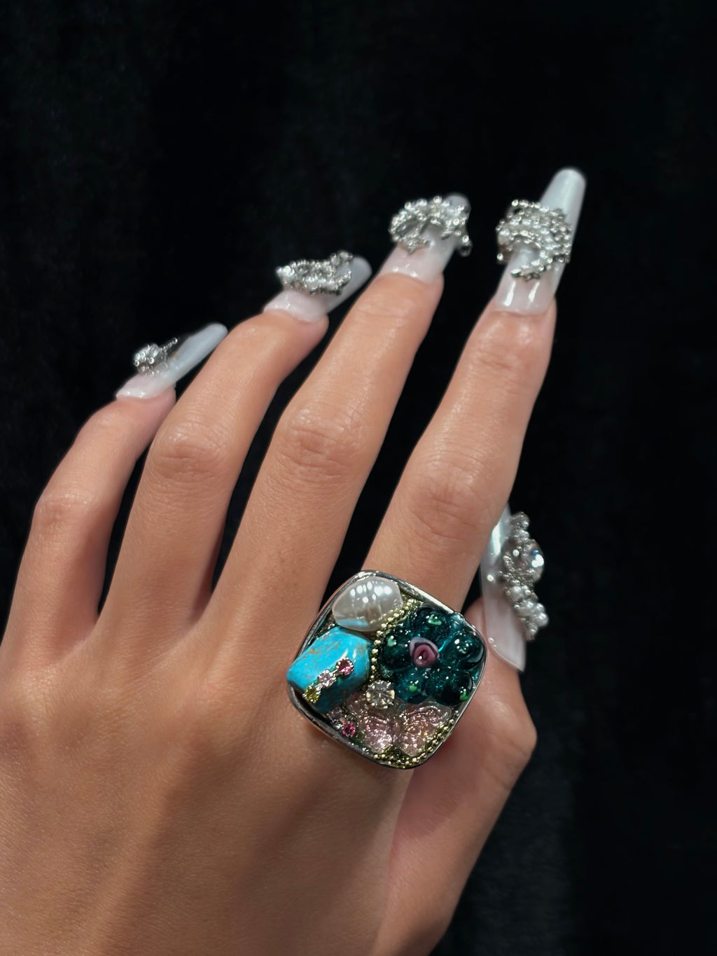 Hand wearing the handcrafted turquoise pearl floral ring with teal flower, turquoise-style stone, pearl and pink decorative details