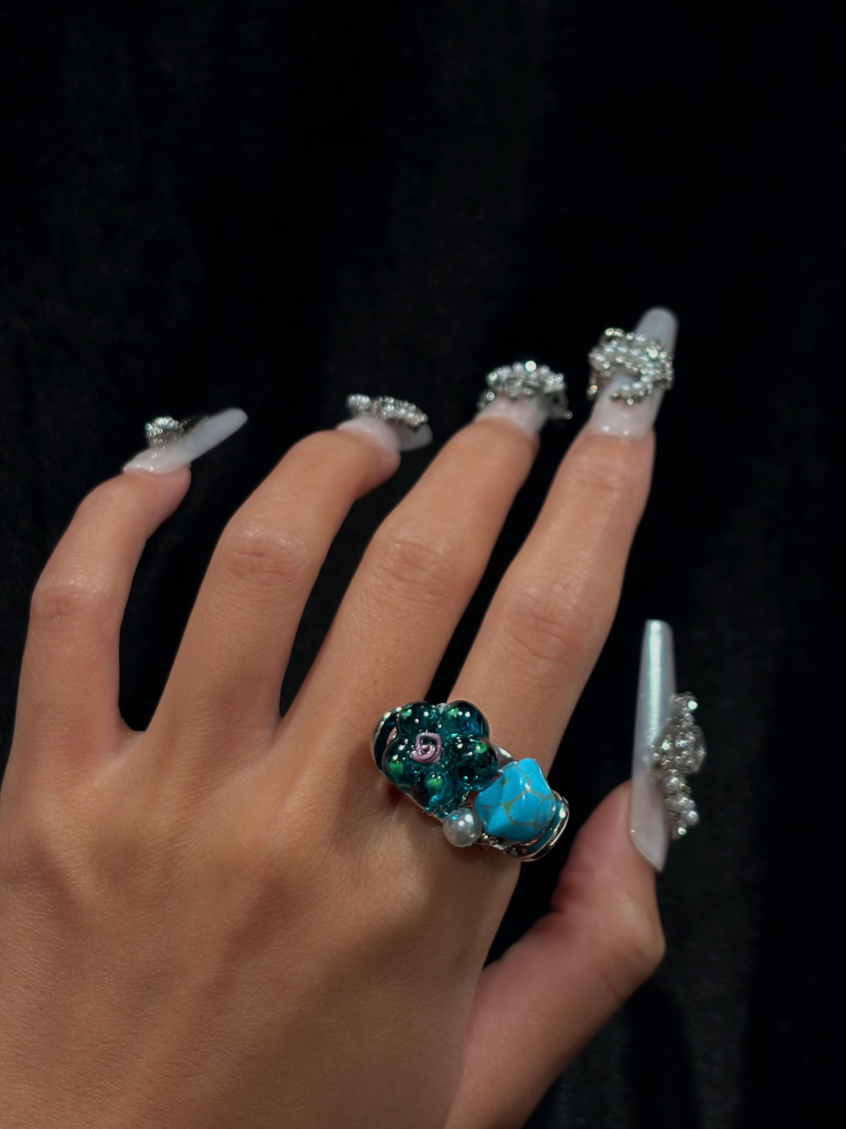Hand wearing the handcrafted turquoise teal flower ring with blue turquoise-style stone, translucent floral beads and pearl accent
