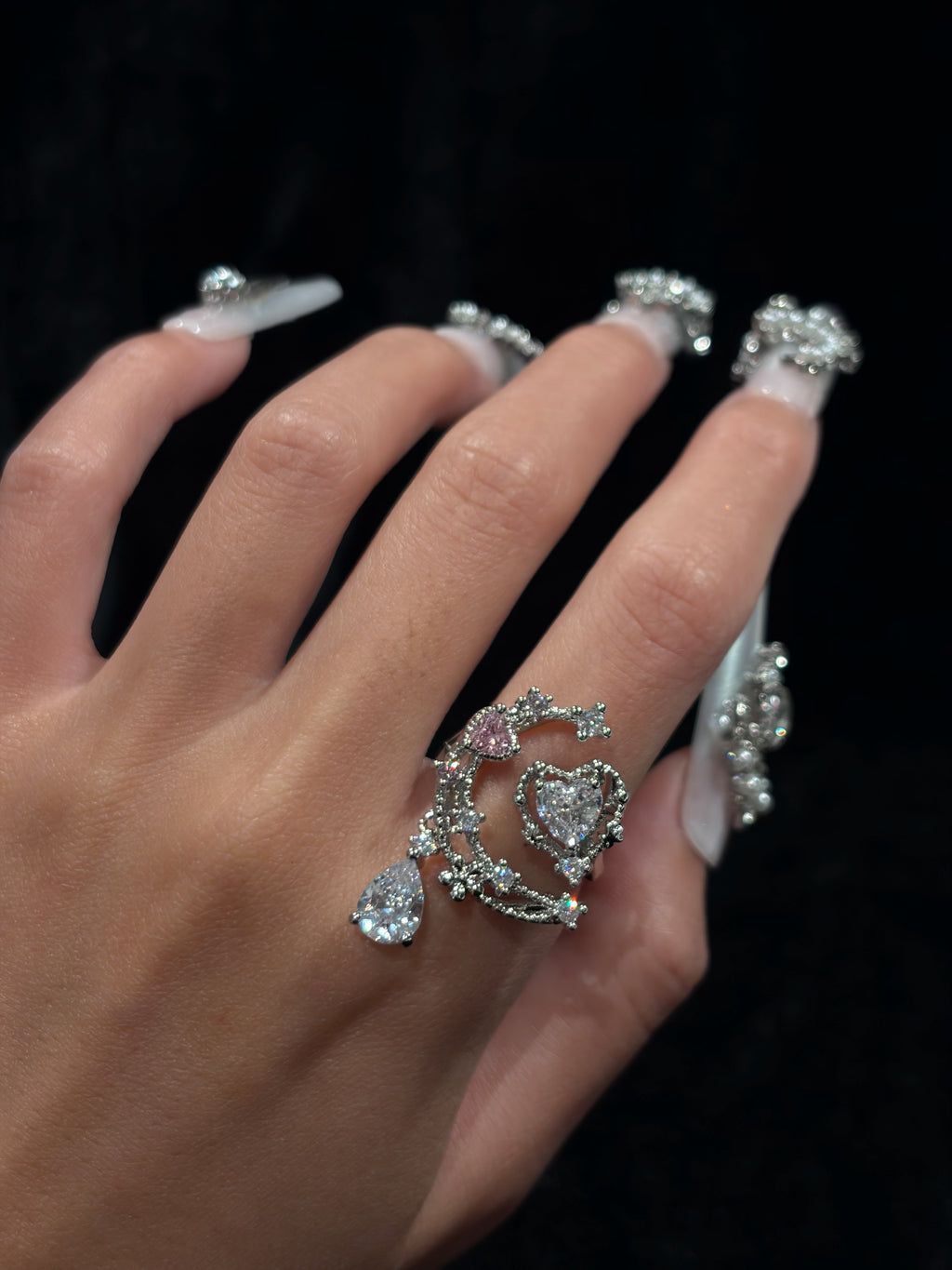 Hand wearing the Moonlit Heart Y2K sparkling adjustable crescent moon ring with heart-shaped crystal and dangling teardrop detail
