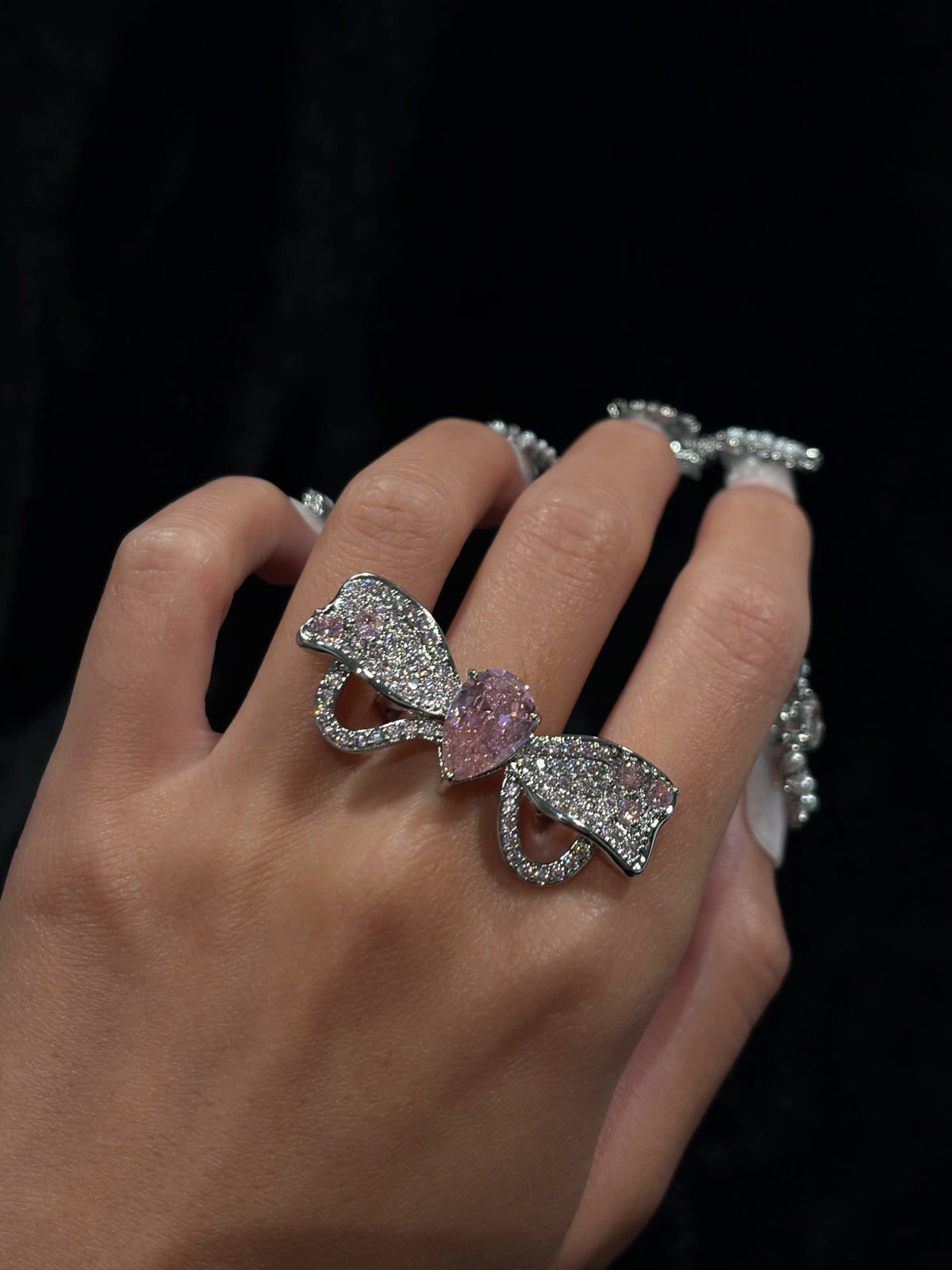 Hand wearing the Radiant Bow Y2K sparkling adjustable statement ring with a large pink pear-shaped crystal and oversized bow design