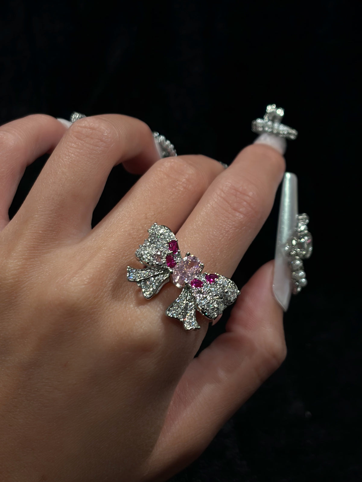 Hand wearing the Roselight Bow Y2K sparkling adjustable ring with pink and clear cubic zirconia bow details against a dark background